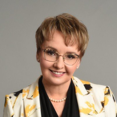 Na zdjęciu widoczna jest kobieta w okularach z krótkimi włosami w białej marynarce w żółto-czarne wzory.